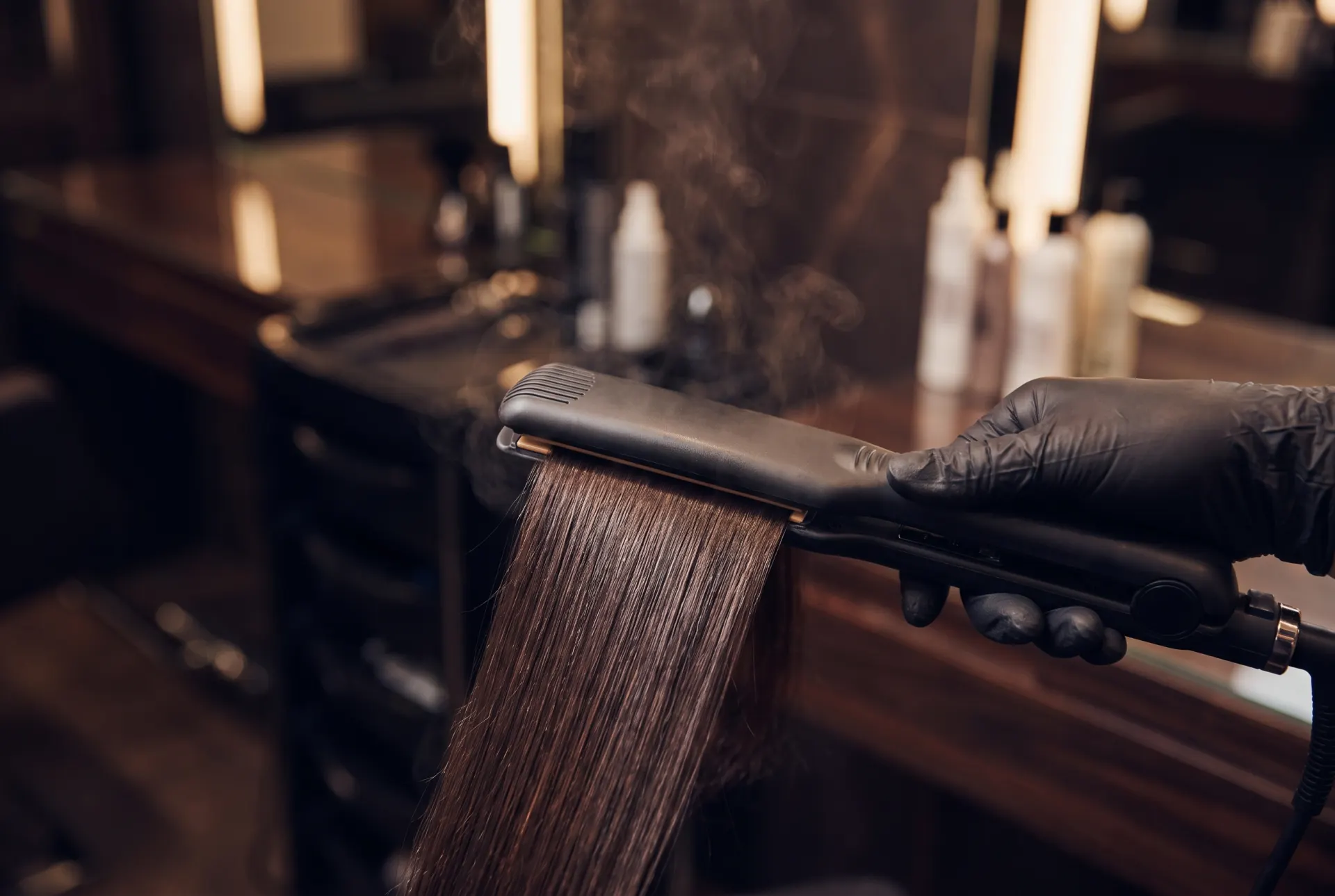 Plattång glider genom glansigt, långt mörkt hår vid keratinbehandling